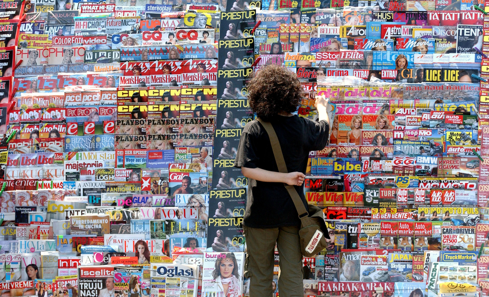 man-standing-in-front-of-magazine-stand-of-headlines